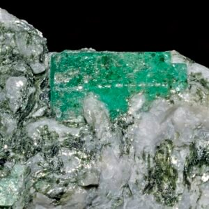 Rough green emerald crystal resting on white host rock
