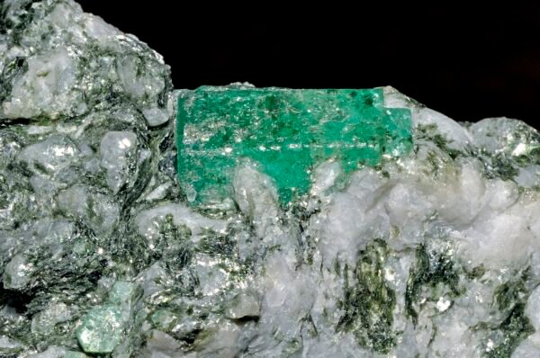 Rough green emerald crystal resting on white host rock